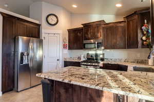 kitchen with vaulted ceiling, dark brown cabinetry, stainless steel appliances, and light granite countertops