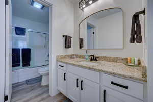 Full bathroom with toilet, wood-type flooring, shower / bath combination with glass door, and vanity