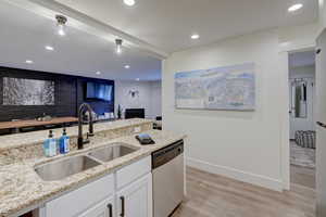 Kitchen with stainless steel dishwasher, light stone countertops, sink, and white cabinets