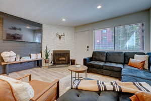 Living room featuring a stone fireplace, a textured ceiling, and light hardwood / wood-style flooring