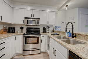 Kitchen with sink, tasteful backsplash, light stone counters, stainless steel appliances, and white cabinets