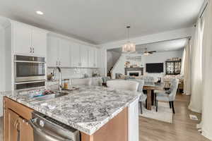 Kitchen featuring sink, light stone counters, an island with sink, stainless steel appliances, and white cabinets