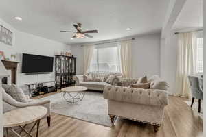 Living room featuring ceiling fan, light hardwood / wood-style flooring, and a textured ceiling