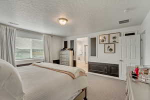 Bedroom with light colored carpet, a textured ceiling, and ensuite bathroom