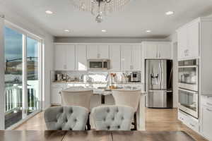 Kitchen featuring white cabinetry, light stone counters, stainless steel appliances, a center island with sink, and light hardwood / wood-style flooring