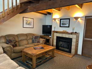 Living room with light colored carpet, beam ceiling, and a tiled fireplace