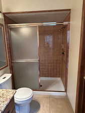 Bathroom with vanity, a shower with shower door, tile patterned floors, and toilet