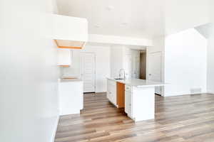 Kitchen featuring light wood-type flooring, sink, an island with sink, and white cabinets