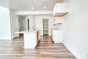 Kitchen featuring an island with sink, sink, white cabinets, and light hardwood / wood-style floors