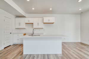 Kitchen featuring white cabinetry, sink, a kitchen island with sink, and light wood-type flooring