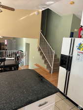 Kitchen with vaulted ceiling, white refrigerator with ice dispenser, white cabinets, and a textured ceiling