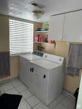 Washroom with cabinets, washer and dryer, light tile patterned floors, and a textured ceiling