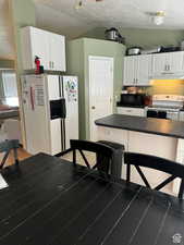 Kitchen featuring white appliances, vaulted ceiling, a textured ceiling, and white cabinets