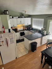 Kitchen with sink, white cabinetry, light hardwood / wood-style flooring, kitchen peninsula, and white appliances