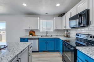 Kitchen featuring blue cabinetry, light stone countertops, sink, and black appliances