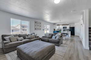 Living room featuring an inviting chandelier, light wood-type flooring, a textured ceiling, and a wealth of natural light