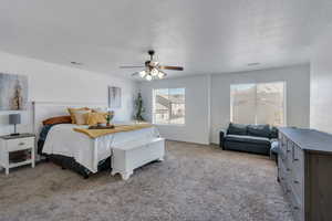 Bedroom with ceiling fan, light colored carpet, and a textured ceiling