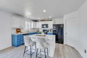 Kitchen with light hardwood / wood-style flooring, black appliances, white cabinets, and a kitchen island