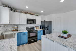 Kitchen with blue cabinetry, sink, white cabinetry, black appliances, and backsplash