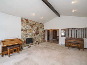 Carpeted living room featuring a stone fireplace and lofted ceiling with beams