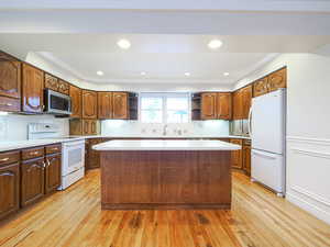 Kitchen with crown molding, white appliances, a center island, and light wood-type flooring