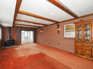 Unfurnished living room with brick wall, carpet, and a wood stove