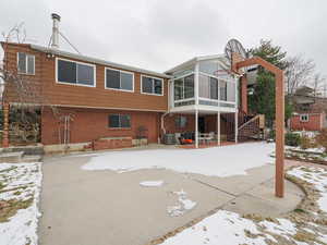 Snow covered back of property featuring a sunroom and cooling unit