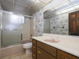 Full bathroom featuring toilet, tile patterned floors, vanity, and bath / shower combo with glass door