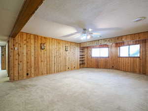 Unfurnished room featuring ceiling fan, wood walls, a textured ceiling, and carpet flooring