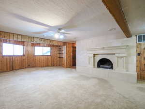 Unfurnished living room featuring wood walls, a textured ceiling, a tile fireplace, beam ceiling, and carpet