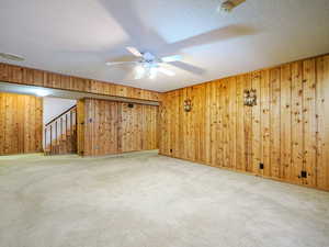 Carpeted spare room with ceiling fan, a textured ceiling, and wood walls