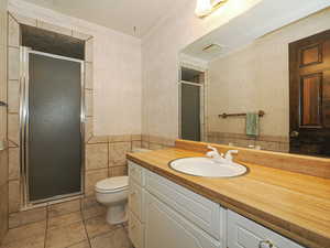 Bathroom featuring toilet, a shower with shower door, tile patterned flooring, and tile walls