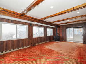 Unfurnished living room featuring wooden walls, a baseboard radiator, carpet flooring, and a wood stove