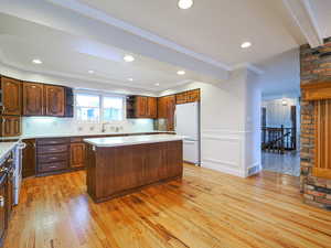 Kitchen featuring sink, ornamental molding, white fridge, a center island, and light hardwood / wood-style floors