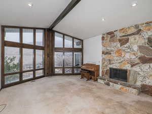 Unfurnished living room with a stone fireplace, vaulted ceiling with beams, floor to ceiling windows, plenty of natural light, and light carpet