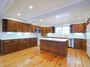 Kitchen featuring crown molding, appliances with stainless steel finishes, a kitchen island, light hardwood / wood-style floors, and decorative backsplash