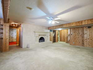 Unfurnished living room with ceiling fan, carpet, a textured ceiling, and wood walls