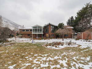 Snow covered back of property with a storage shed, a mountain view, and a sunroom