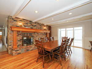 Dining area featuring beamed ceiling, crown molding, light hardwood / wood-style floors, and a brick fireplace