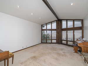 Living room with high vaulted ceiling, light carpet, beam ceiling, and a wall of windows