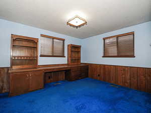 Unfurnished office with dark carpet, built in desk, a textured ceiling, and wood walls