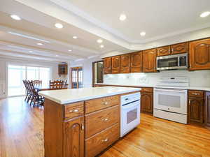 Kitchen with tasteful backsplash, light wood-type flooring, ornamental molding, beamed ceiling, and white appliances