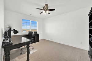 Carpeted home office featuring ceiling fan