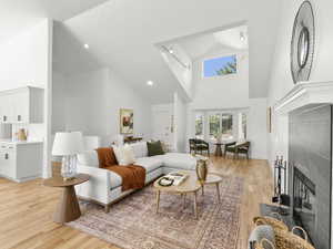 Living room with a tiled fireplace, high vaulted ceiling, and light hardwood floors