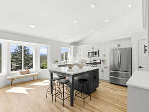 Kitchen with a breakfast bar area, appliances with stainless steel finishes, a center island, white cabinets, and light hardwood flooring