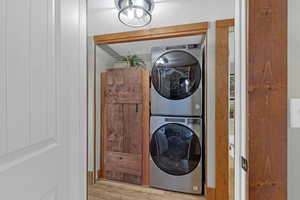 Clothes washing area featuring light hardwood / wood-style floors and stacked washer / dryer