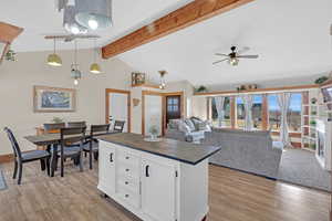 Kitchen with butcher block countertops, vaulted ceiling with beams, white cabinets, hanging light fixtures, and light wood-type flooring