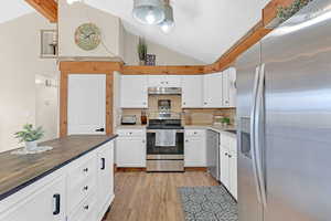 Kitchen featuring stainless steel appliances, white cabinetry, wood counters, and lofted ceiling with beams