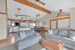 Living room with ceiling fan with notable chandelier, wood-type flooring, sink, and lofted ceiling with beams