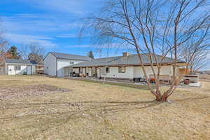 Back of house featuring a hot tub, a patio, an outdoor structure, and a lawn